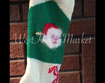 May include: A white, green and red knitted Christmas stocking with the name "ALLI" embroidered on the front. The stocking has a Santa Claus face and a candy cane design.