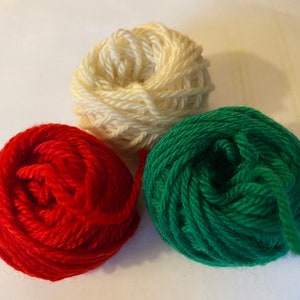 May include: Three balls of yarn in red, white, and green. The yarn is wound into balls.