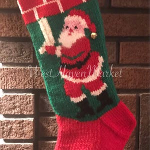 May include: A red and green knitted Christmas stocking with a Santa Claus design. The stocking has a white cuff with the name "KEN" embroidered on it.