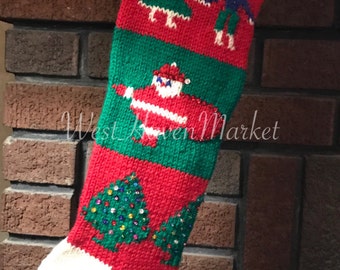 May include: Hand-knitted Christmas stocking in red, green, and white. The top features the name "PIPER" in green letters on a white background. The stocking is decorated with images of Santa Claus, Christmas trees, and figures.