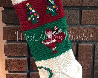 May include: A green, white and red knitted Christmas stocking with a bell at the bottom. The stocking has a white band with the number "20" on it, and a red band with two green Christmas trees decorated with sequins. The stocking also has a green band with a red Santa Claus figure holding a bag of gifts. The stocking is hanging on a brick fireplace.