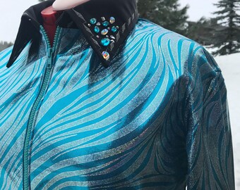 May include: A long-sleeve zip-up shirt featuring a metallic turquoise and silver swirling pattern. The garment has a solid black collar adorned with a cluster of iridescent blue and clear crystals on the left side and a teal front zipper.