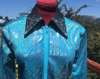 May include: A turquoise, shimmering jacket with a zebra stripe pattern. The jacket has a black collar with silver and blue embellishments and a full-length zipper. The jacket is displayed on a mannequin against a backdrop of trees and a blue sky.