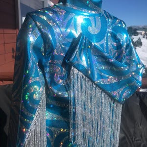 May include: A turquoise and silver sequined show shirt with silver fringe on the sleeves.