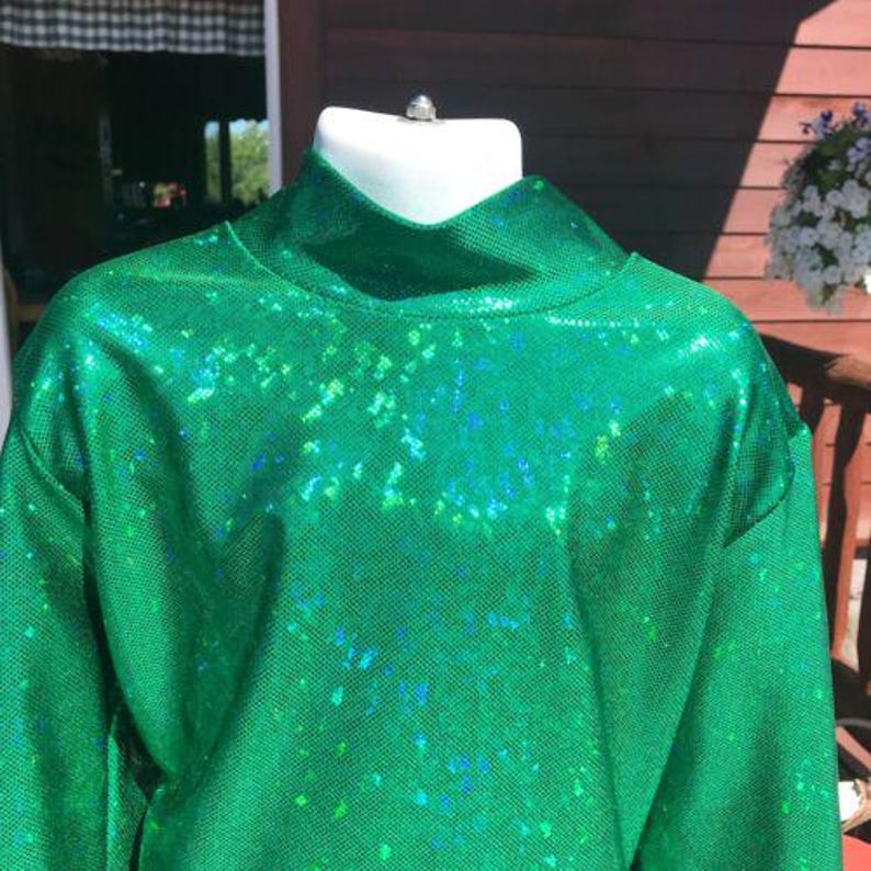 May include: A green top with a high neckline, displayed on a white mannequin. The fabric has a textured appearance with iridescent blue and green flecks. The long-sleeved top is a vibrant, eye-catching piece of clothing.