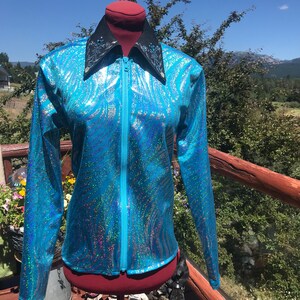 May include: A turquoise zip-up jacket with a shimmering, iridescent finish. The jacket features a black collar with silver embellishments and a full-length zipper. The long-sleeved jacket has a unique, wavy pattern.
