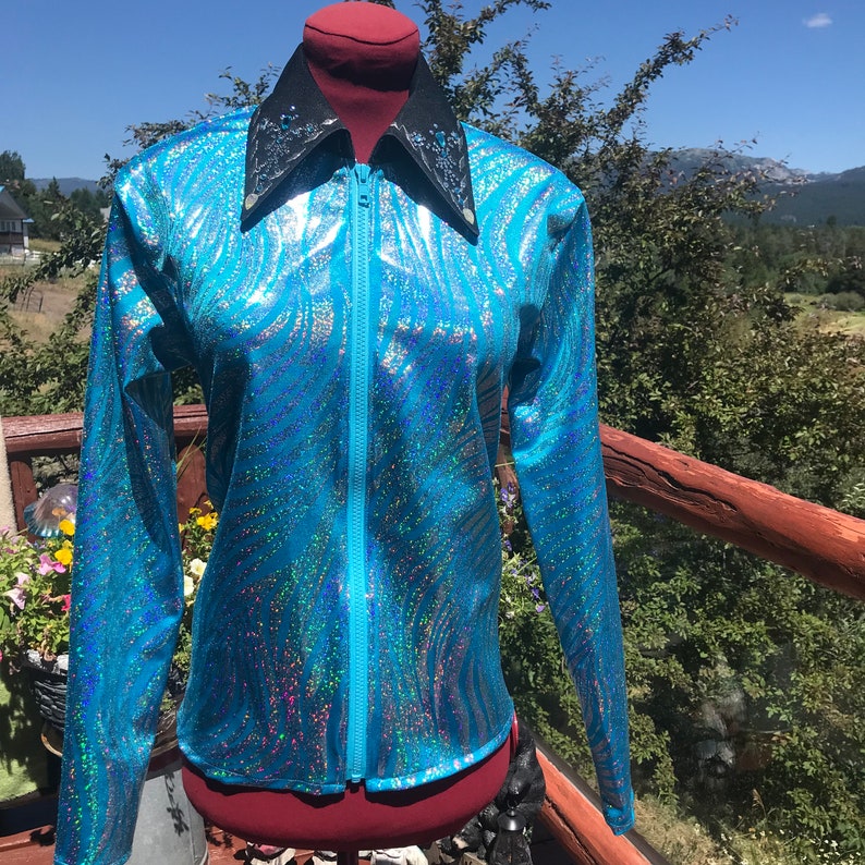 May include: A turquoise zip-up jacket with a shimmering, iridescent finish. The jacket features a black collar with silver embellishments and a full-length zipper. The long-sleeved jacket has a unique, wavy pattern.