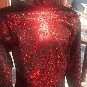 May include: A red long-sleeved shirt with a black and silver abstract pattern. The shirt has a mock neck.