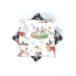 May include: A square quilted pot holder with a white background featuring a colorful cartoon print of characters and scenes. The edges are black with white snowflake patterns. The pot holder is designed to protect surfaces from heat.