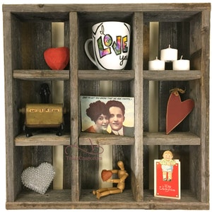 May include: A rustic wooden shelf with nine compartments, each filled with various Valentine's Day themed items. The top center compartment features a white mug with the word "LOVE" written in rainbow colors. The other compartments contain items such as hearts, candles, a vintage calendar, a postcard, and a small wooden figurine.