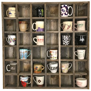 May include: A rustic wooden mug rack with 18 compartments, each holding a different ceramic mug. The mugs feature various designs, including a cartoon alien, a giraffe, a heart with the word "love", and a mug with the word "DALI".