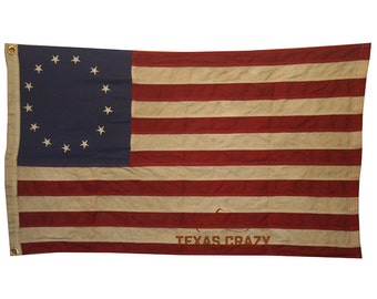May include: A vintage-style flag featuring a blue canton with 13 white stars arranged in a circle, and alternating red and white stripes. The flag has a distressed appearance and the text "TEXAS CRAZY" is printed on the bottom.