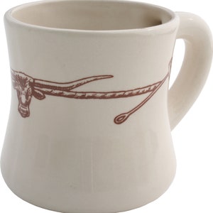 May include: A white ceramic mug with a brown design of a longhorn steer's head and horns. The mug has a wide, rounded base and a handle.