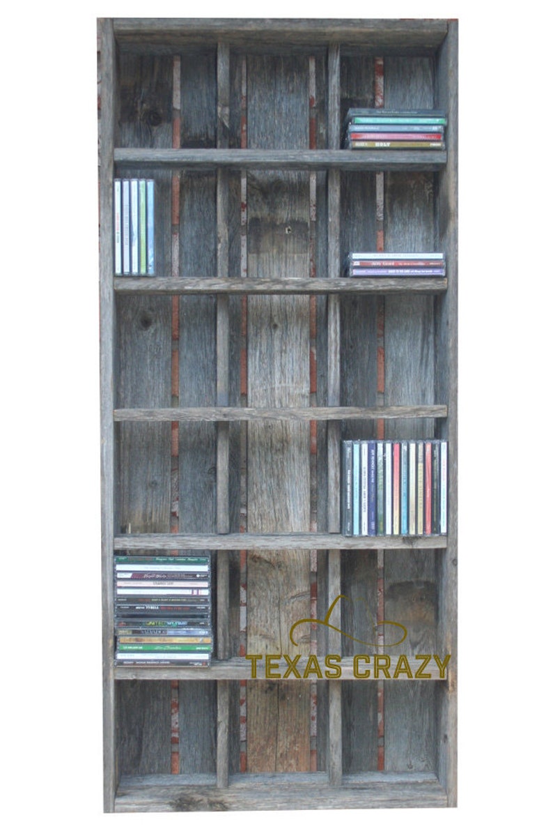 Puede incluir: Estanter&iacute;a r&uacute;stica de madera para CD con m&uacute;ltiples estantes, que muestra varios CD. La estanter&iacute;a est&aacute; hecha de madera envejecida con una mezcla de tonos grises y marrones. El texto "TEXAS CRAZY" es visible en la parte delantera.