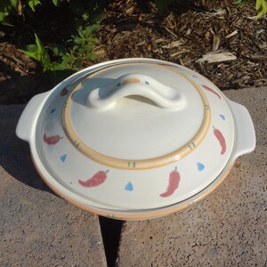Pu&ograve; includere: Piatto da forno in ceramica bianca con coperchio. Il piatto ha un design con peperoncini rossi, arancioni e verdi. Il coperchio ha un manico.