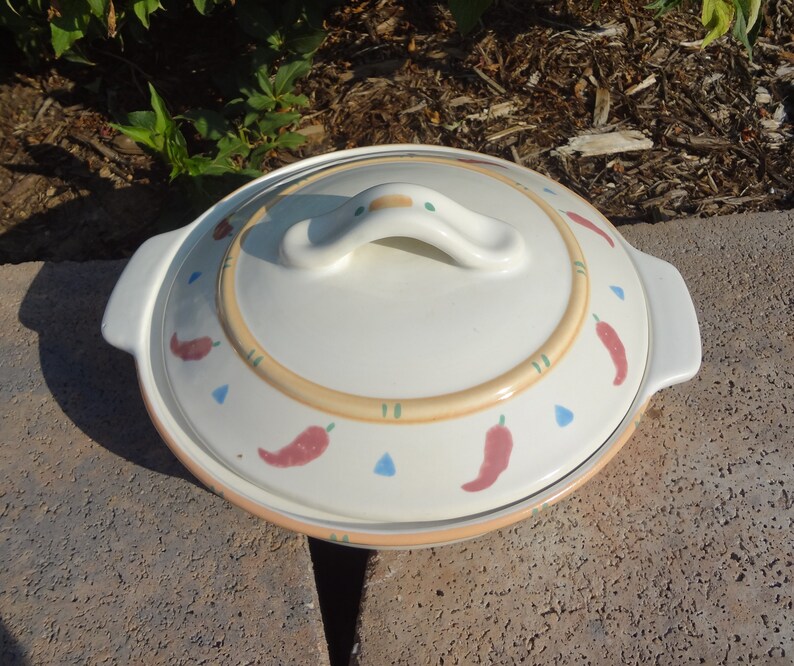 Pu&ograve; includere: Piatto da forno in ceramica bianca con coperchio. Il piatto ha un design con peperoncini rossi, arancioni e verdi. Il coperchio ha un manico.