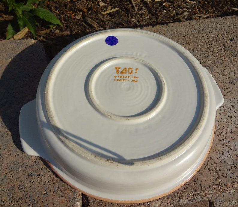 Pu&ograve; includere: Piatto da forno in ceramica bianca con due manici e un bordo marrone. Sul fondo del piatto &egrave; presente un adesivo dorato con la scritta "Treasure Craft - USA".