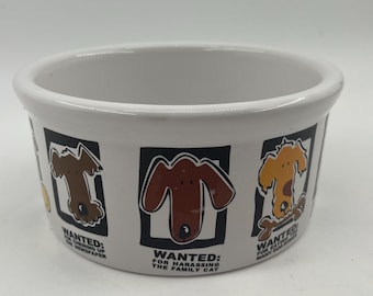Puede incluir: Cuenco para mascotas de cerámica blanca con un diseño de borde negro con ilustraciones de perros de dibujos animados. El cuenco tiene texto que dice "WANTED" con varias descripciones humorísticas, como "por masticar el periódico".