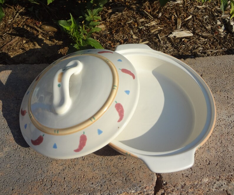 Pu&ograve; includere: Piatto da forno in ceramica bianca con coperchio. Il piatto e il coperchio sono decorati con peperoncini rossi e un bordo marrone e verde.