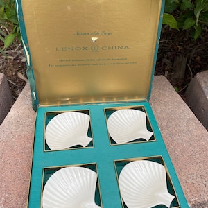 May include: Set of four white Lenox china shell-shaped ash trays in a green and gold box. The box lid reads "Nassau Ash Trays" and "LENOX CHINA". The text below reads "Matched miniature shells, individually handcrafted. The imaginative and decorative touch for dinner, bridge or end tables."