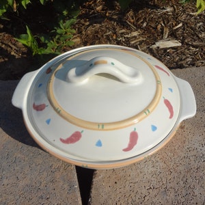 Pu&ograve; includere: Piatto da forno in ceramica bianca con coperchio. Il piatto ha un design con peperoncini rossi, arancioni e verdi. Il coperchio ha un manico.