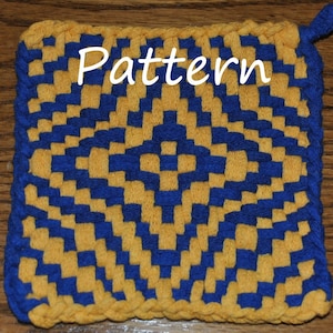 Puede incluir: Un posavasos tejido con un patrón de cuadrados amarillos y azules alternados. El posavasos tiene un borde de flecos y un lazo para colgar.