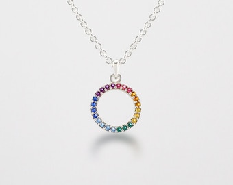 May include: A silver necklace with a rainbow circle pendant. The circle is made of small gemstones in shades of red, orange, yellow, green, blue, and purple.