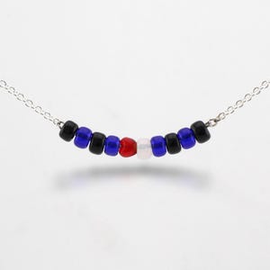 May include: A delicate necklace featuring a series of small, colorful beads. The beads are arranged in a row, with a pattern of black, blue, red, and white. The necklace is strung on a fine silver chain, creating a simple yet eye-catching design.