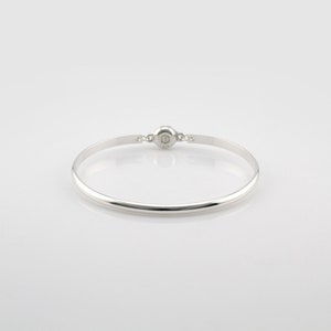Puede incluir: Un brazalete de plata con cierre de bisagra. El brazalete es liso y pulido.
