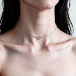 May include: A silver-toned choker necklace featuring a delicate chain with small, uniform circular links. The necklace is centered by a single, small, circular ring pendant that connects the two sides of the chain, resting against the base of the neck.