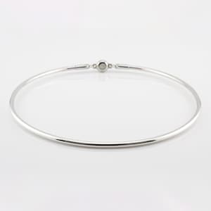 May include: A silver-colored choker necklace with a simple, minimalist design. The necklace is a smooth, thin band that forms a complete circle, with a small clasp at the back. The jewelry is displayed on a white background.