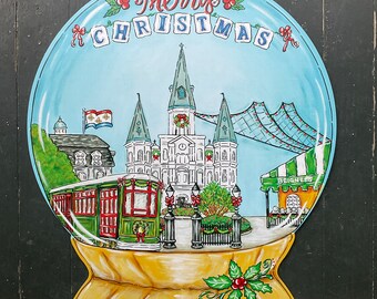 Könnte beinhalten: Ein blauer und weißer Schneekugel mit einer gemalten Szene der St. Louis Cathedral in New Orleans, Louisiana. Die Kugel hat eine goldene Basis und eine rote Schleife. Der Text "Merry Christmas" ist in roten Buchstaben auf der Kugel geschrieben.