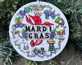 May include: A white round ornament with a colorful illustration of Mardi Gras symbols, including a red crawfish, a purple, green, and gold mask, a jester, and the words "Mardi Gras".
