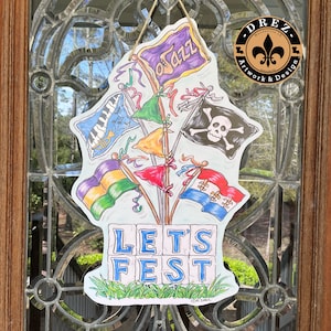 May include: A colorful door hanger with the words "Let's Fest" in blue letters on a white background. The hanger features a variety of flags with musical notes, a skull and crossbones, and other festive designs.