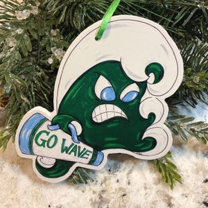 May include: A Christmas ornament featuring a cartoon character with a green body, white hair, and blue eyes. The character is holding a megaphone that says "GO WAVE" in blue and white. The ornament is hanging from a green ribbon.