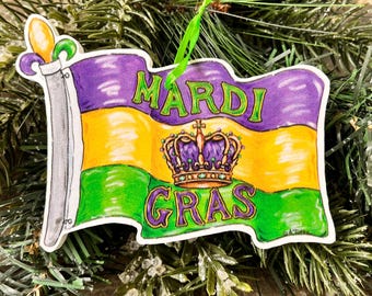 May include: A Mardi Gras flag ornament with a purple, gold, and green design. The flag features a crown with a fleur-de-lis on top and the words "Mardi Gras" written in green.