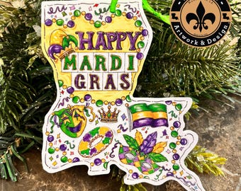 May include: A white wooden ornament shaped like the state of Louisiana with a colorful design. The ornament features the words "Happy Mardi Gras" in a purple, yellow, and green color scheme. The ornament is decorated with beads, masks, and other Mardi Gras symbols.
