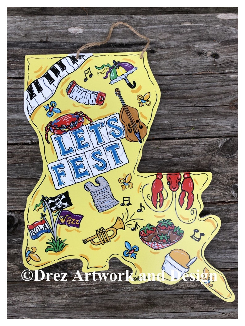 Op de afbeelding: Een geel houten bord in de vorm van de staat Louisiana met de woorden "Let's Fest" in blauwe en witte letters. Het bord is versierd met verschillende afbeeldingen die verband houden met New Orleans, waaronder een piano, een trompet, een krab, een fleur-de-lis, een noot, een piratenvlag, een mand met aardbeien en een bol ijs.