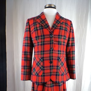 May include: A vintage red plaid skirt suit. The jacket has a notched collar, two front pockets, and three black buttons. The skirt is a matching red plaid pattern. The suit is displayed on a mannequin.