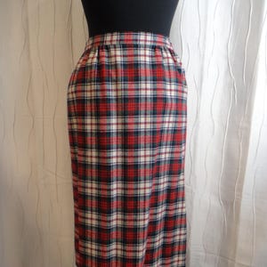 May include: A plaid pencil skirt in red, white, and navy blue. The skirt is displayed on a mannequin, showcasing its classic, knee-length design. The fabric features a traditional tartan pattern, suitable for various occasions.