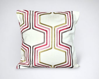 May include: White square throw pillow with a geometric pattern embroidered in pink, red, and gold thread.
