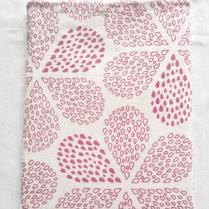 Puede incluir: Una funda rectangular de tela con una base de color blanco roto y un patr&oacute;n repetitivo de formas de gotas de color rosa. Las gotas est&aacute;n dispuestas en grupos que forman motivos m&aacute;s grandes similares a p&eacute;talos sobre el tejido.