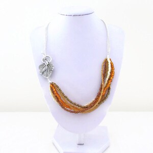 Op de afbeelding: Een meerstrengs ketting met bruine, oranje en cr&egrave;me kralen. De ketting heeft een zilveren bladeren hanger.