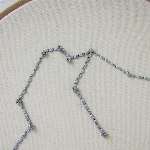 May include: A silver glitter embroidery of the Aquarius constellation on a white fabric background.