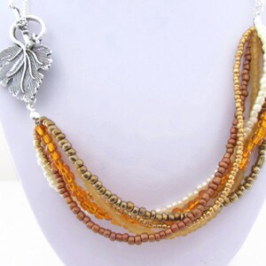 Op de afbeelding: Een meerstrengs ketting met een zilveren bladeren hanger. De ketting is gemaakt van kleine kralen in tinten goud, bruin en wit.