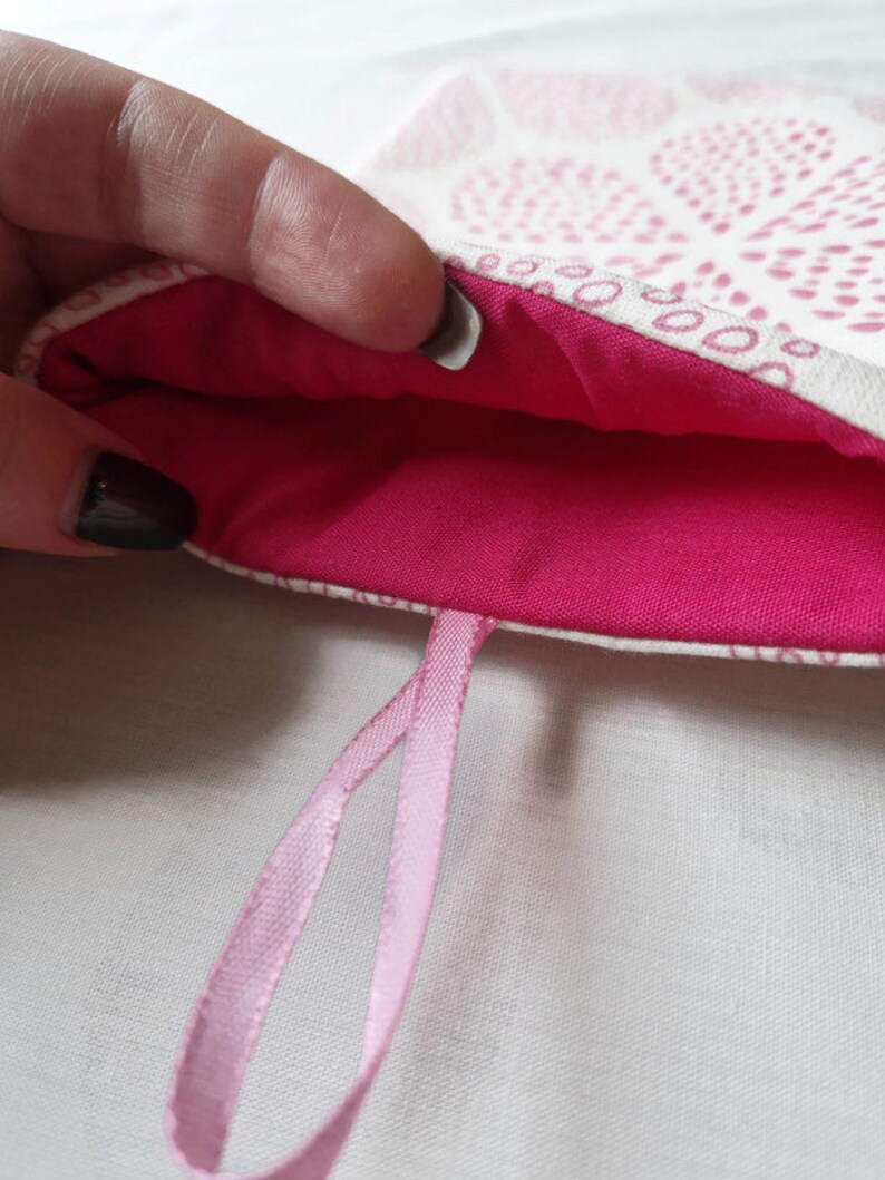 Puede incluir: Una bolsa de tela con un exterior de color crema con un patr&oacute;n repetitivo de puntos rosas y un forro interior de color rosa intenso. La bolsa incluye un lazo de cinta rosa claro unido al borde inferior para colgarla o transportarla.