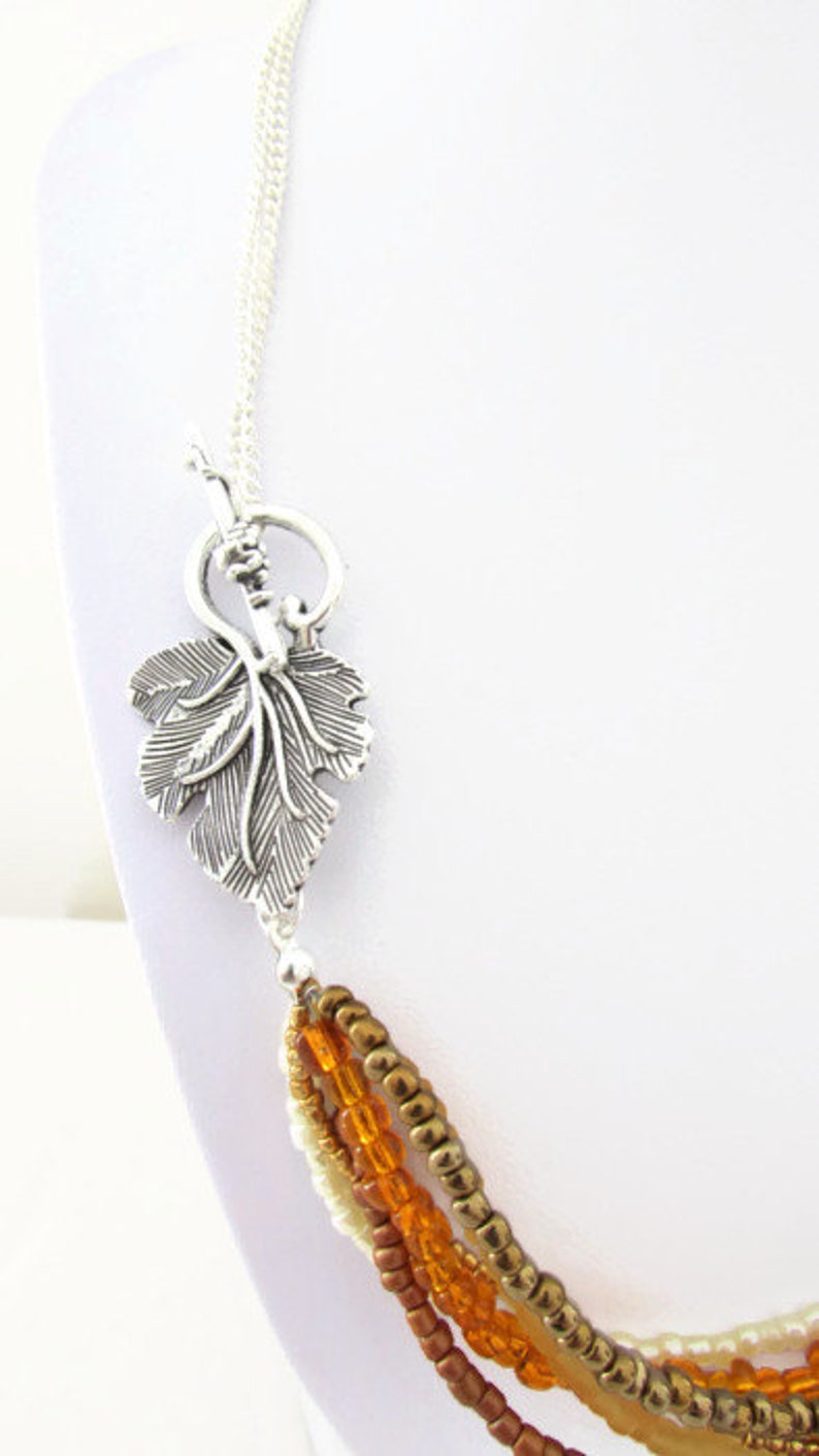 Op de afbeelding: Een meerstrengs ketting met een zilveren bladsluiting. De ketting heeft vier strengen kralen in tinten bruin, oranje en cr&egrave;me.