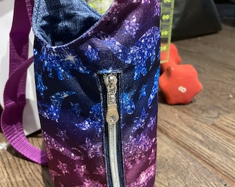 May include: A purple and blue fabric bag with a zipper closure and a purple strap. The bag has a galaxy print with stars and a dinosaur silhouette.
