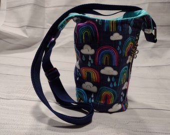 May include: A small blue crossbody bag with a rainbow and cloud print. The bag has a navy blue strap and a zipper closure with a decorative charm.
