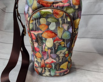 Op de afbeelding: Een crossbodytas met een kleurrijk paddenstoelenpatroon. De tas heeft een bruine verstelbare riem, een voorvak met ritssluiting en een bronzen rits. De binnenkant van de tas is gevoerd met een contrasterende oranje stof.